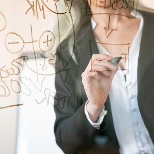 Unrecognizable grey-haired businesswoman writing on glass board. Hand holding black marker and making notes for project. Strategy, business and management concept